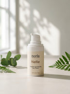 Nellie Peptide Age-Defying Eye Cream 15 ml by Norla, small airless pump bottle on a marble surface with eucalyptus and fern